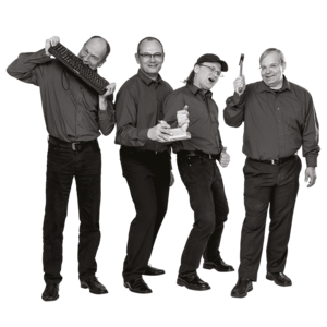 Vier Männer in dunklen Hemden und Hosen stehen nebeneinander, einer hält eine Tastatur, ein anderer einen Schraubendreher, zwei zeigen Daumen hoch.