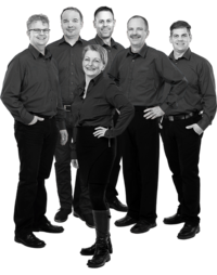 Sechs Personen in schwarzer Arbeitskleidung stehen zusammen, eine Frau vorne mit Hand in der Hüfte, fünf Männer im Hintergrund, alle in Hemden und Hosen.