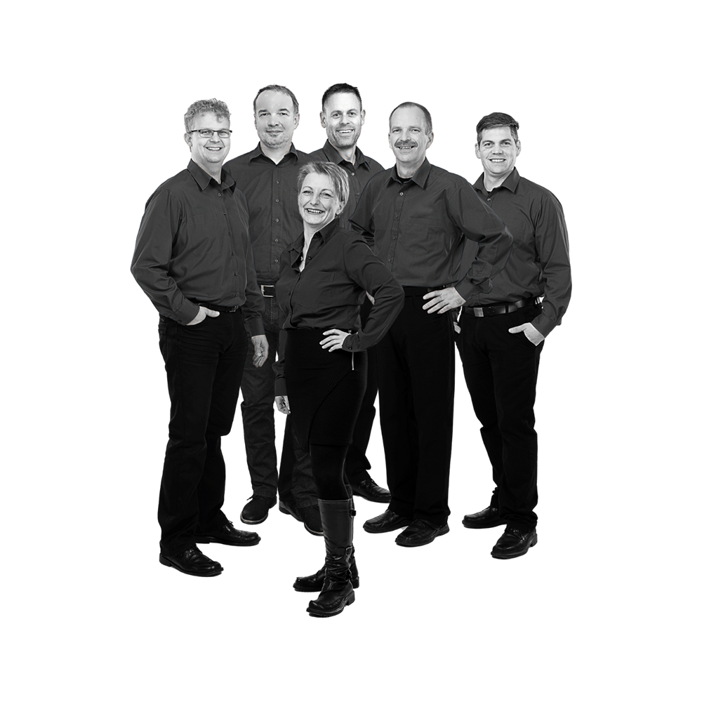 Sechs Personen in schwarzer Arbeitskleidung stehen zusammen, eine Frau vorne mit Hand in der Hüfte, fünf Männer im Hintergrund, alle in Hemden und Hosen.